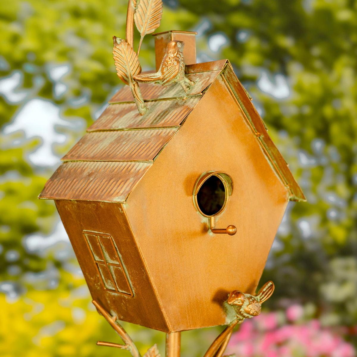 Copper birdhouse with decorative elements against a blurred natural background