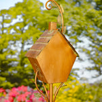 Decorative copper birdhouse with leaf accents against a blurred garden background