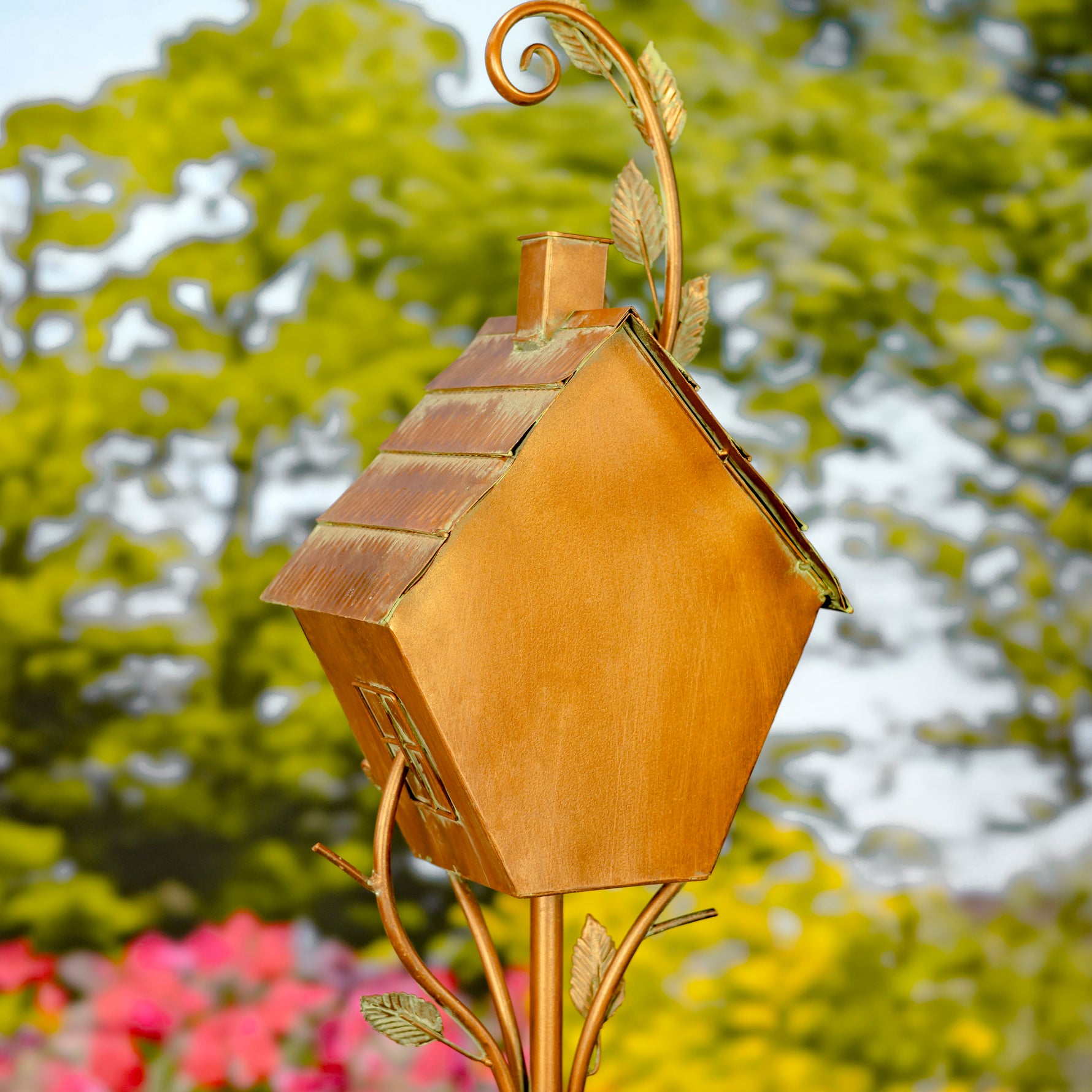 Decorative copper birdhouse with leaf accents against a blurred garden background