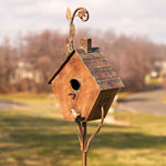 Decorative metal birdhouse on a stand with a blurred outdoor background