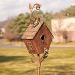 Decorative copper birdhouse on a stand with a blurred outdoor background