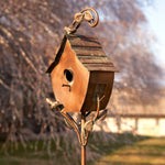 Decorative copper birdhouse on a stand with a blurred garden background