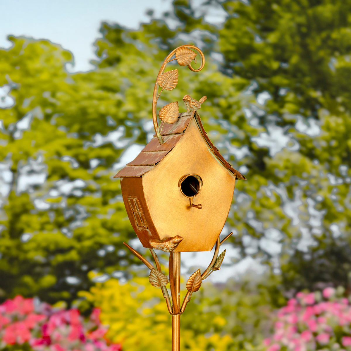 Decorative gold birdhouse on a stand with a blurred green and pink garden background