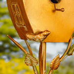 Gold birdhouse with decorative elements against a blurred natural background
