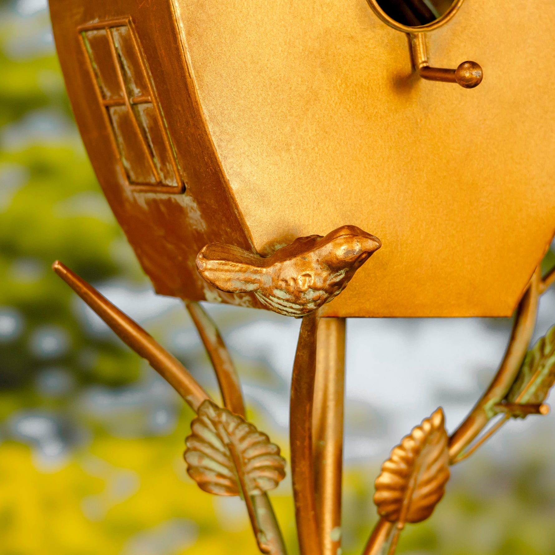 Gold birdhouse with decorative elements against a blurred natural background