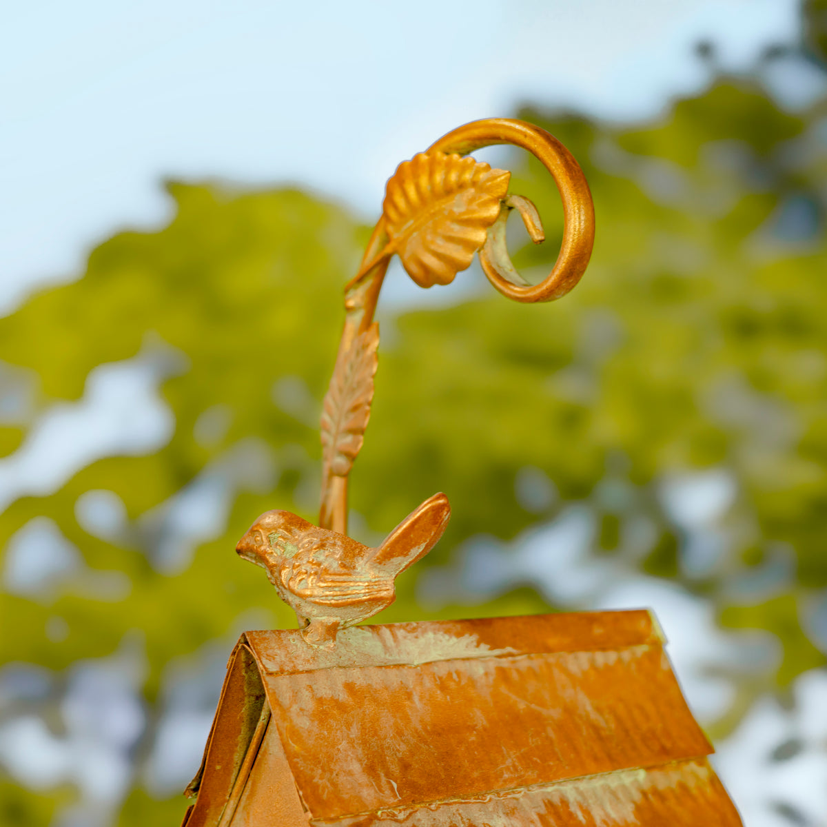 Decorative metal sculpture with a bird and leaf design against a blurred natural background