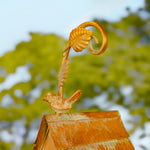Decorative metal sculpture with a bird and leaf design against a blurred natural background
