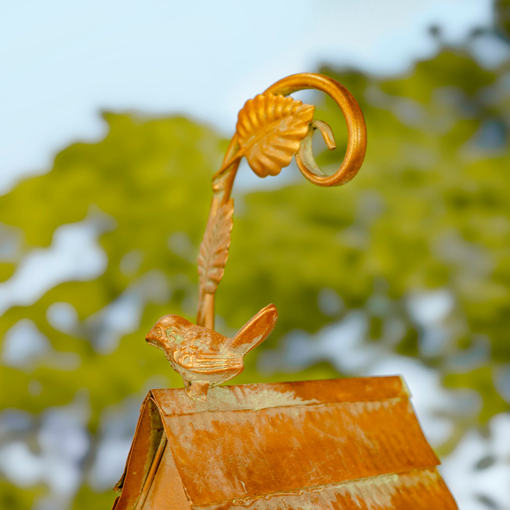 Decorative metal sculpture with a bird and leaf design against a blurred natural background