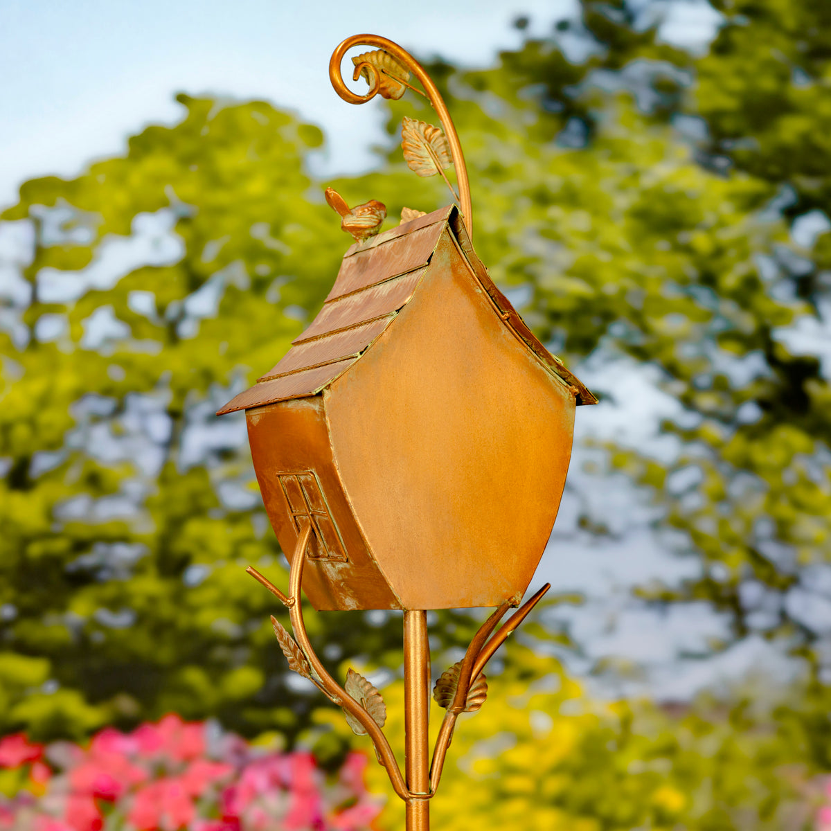 Decorative gold birdhouse on a stand with a blurred natural background