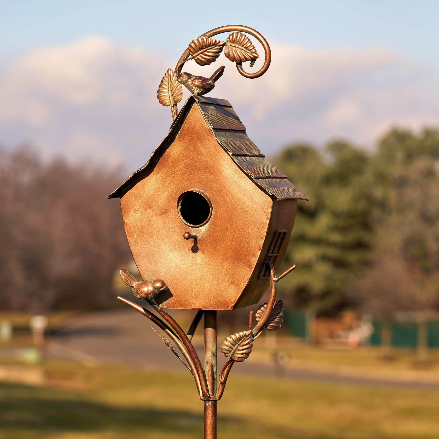Decorative copper birdhouse on a stand with a blurred natural background