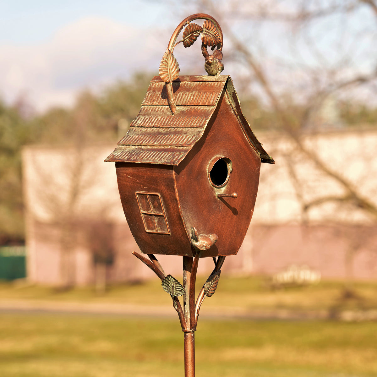 Decorative copper birdhouse on a stand with a blurred outdoor background