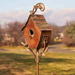 Decorative copper birdhouse on a stand with a blurred outdoor background