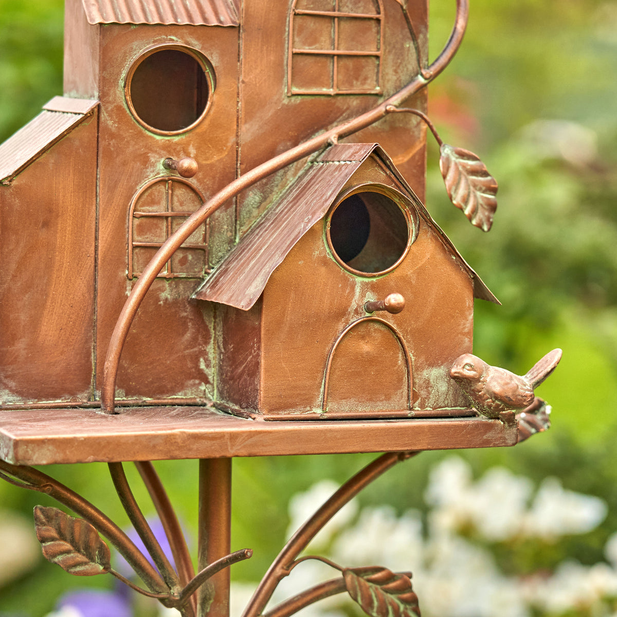 Copper birdhouse with a bird perched on it, set against a blurred natural background.