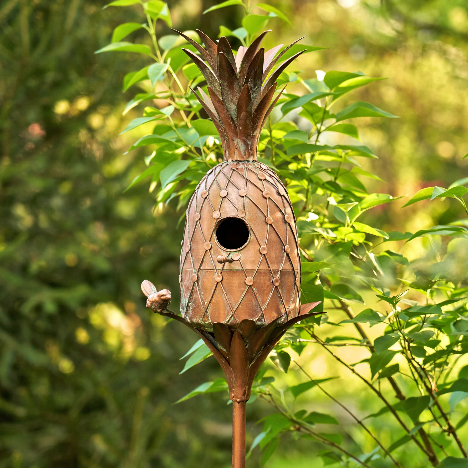 Pineapple-shaped birdhouse on a stand with green foliage in the background