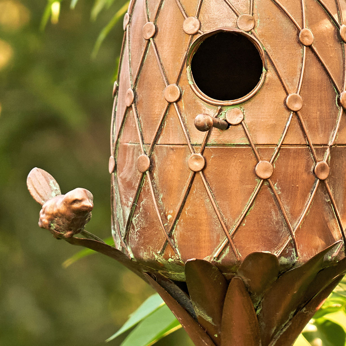 Decorative copper birdhouse with intricate patterns on a blurred green background