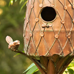 Decorative copper birdhouse with intricate patterns on a blurred green background