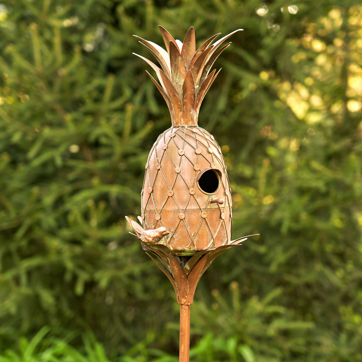 Pineapple-shaped birdhouse on a stand with a green foliage background
