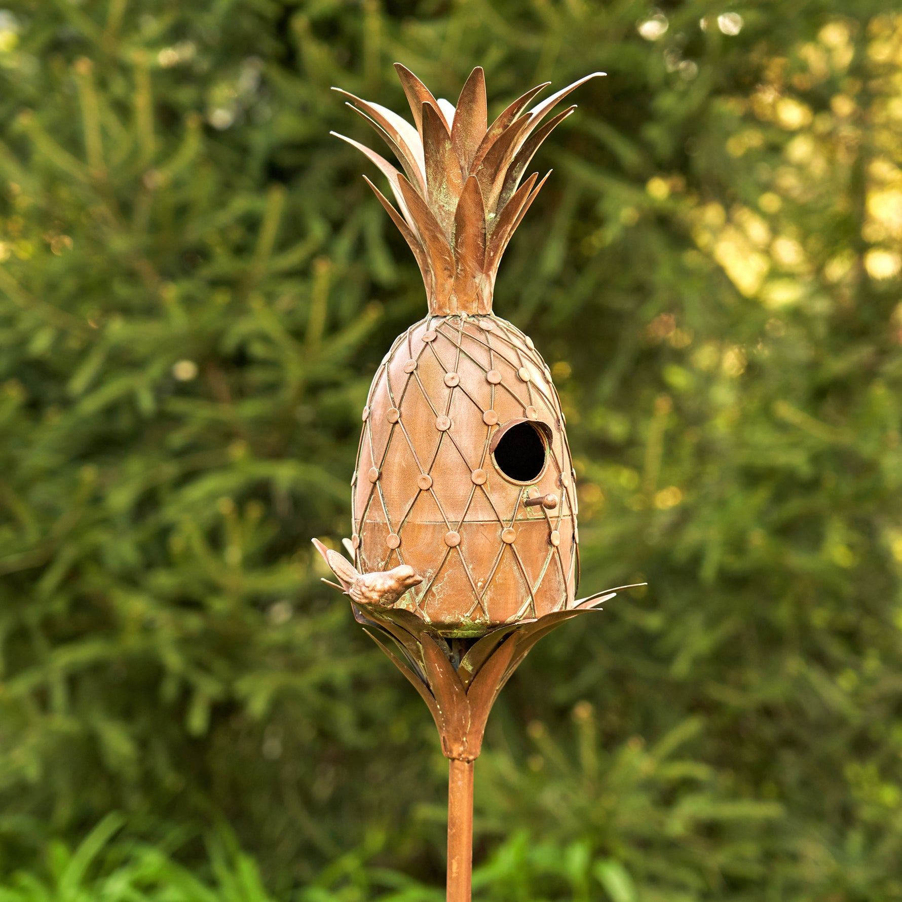 Pineapple-shaped birdhouse on a stand with a green foliage background