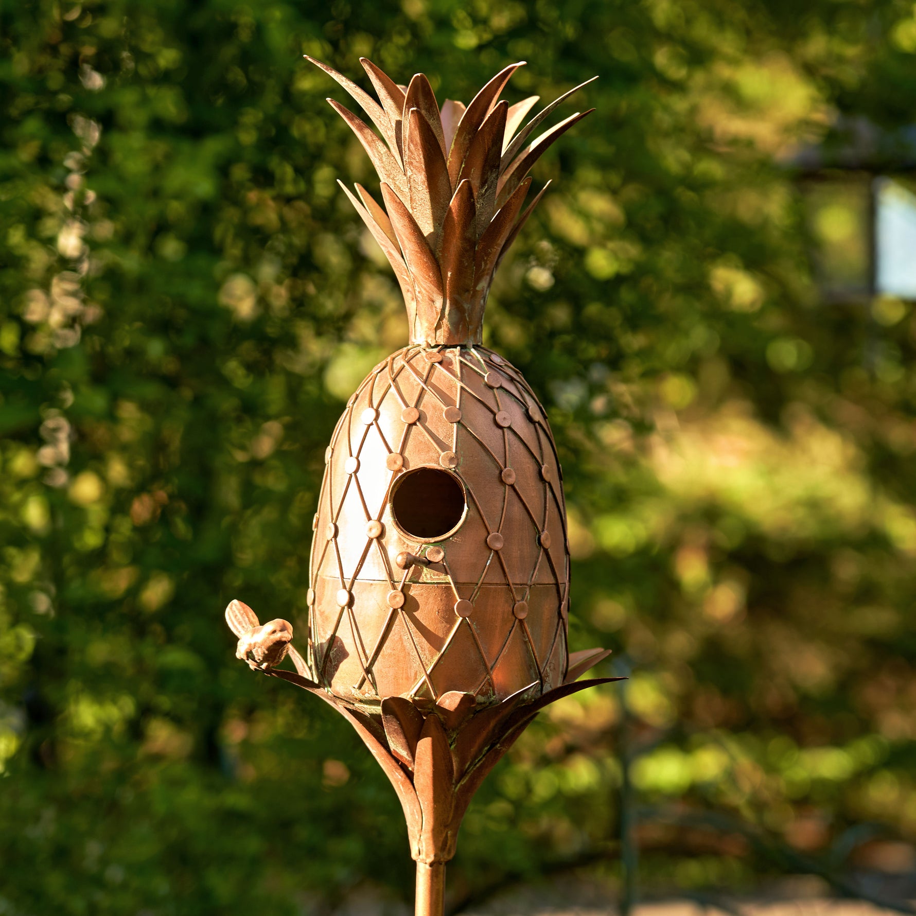 Bronze pineapple-shaped birdhouse with a blurred green background