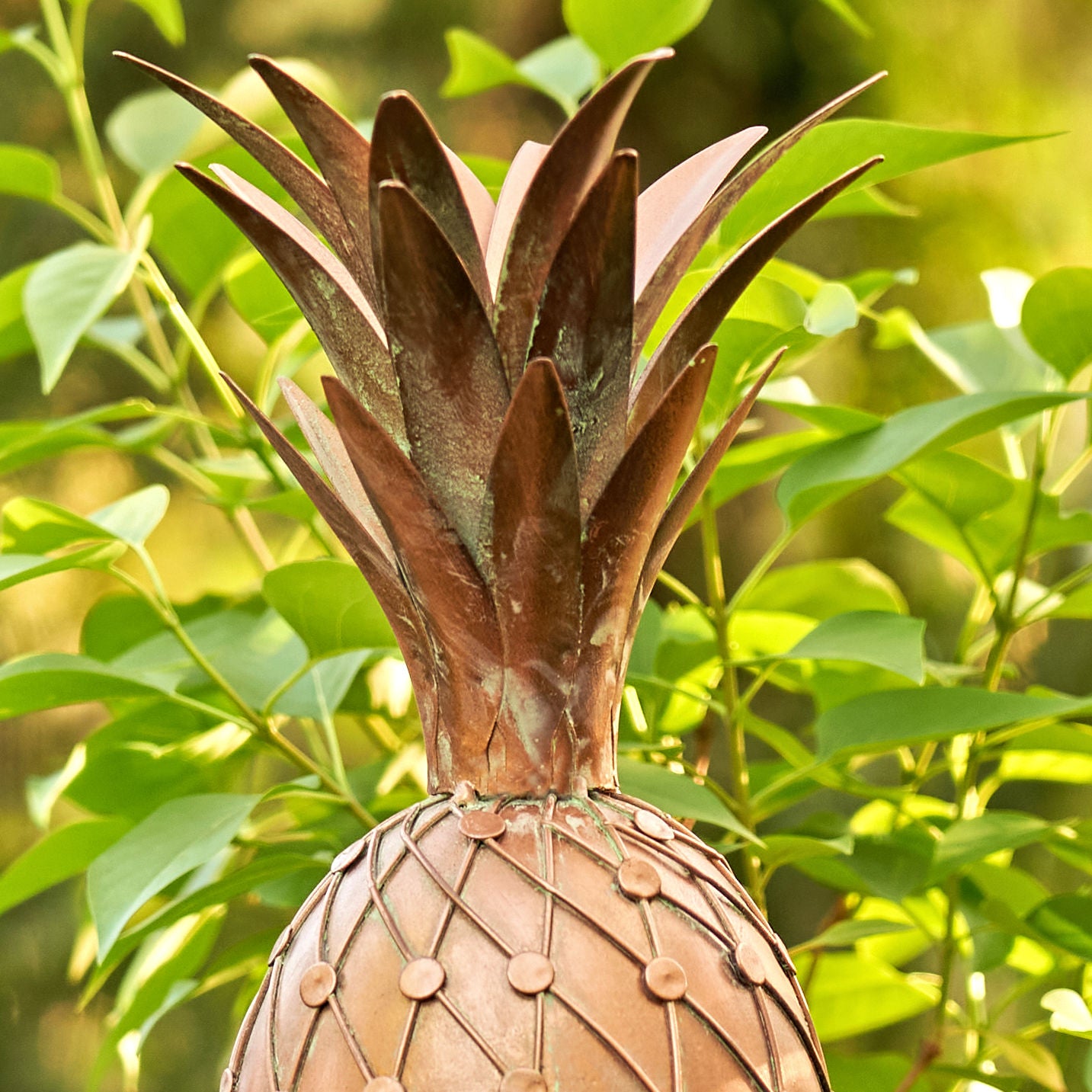 Decorative metal pineapple against a green leafy background