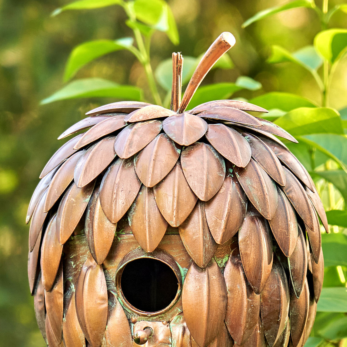 Decorative birdhouse shaped like a pine cone with a blurred green foliage background