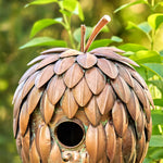 Decorative birdhouse shaped like a pine cone with a blurred green foliage background