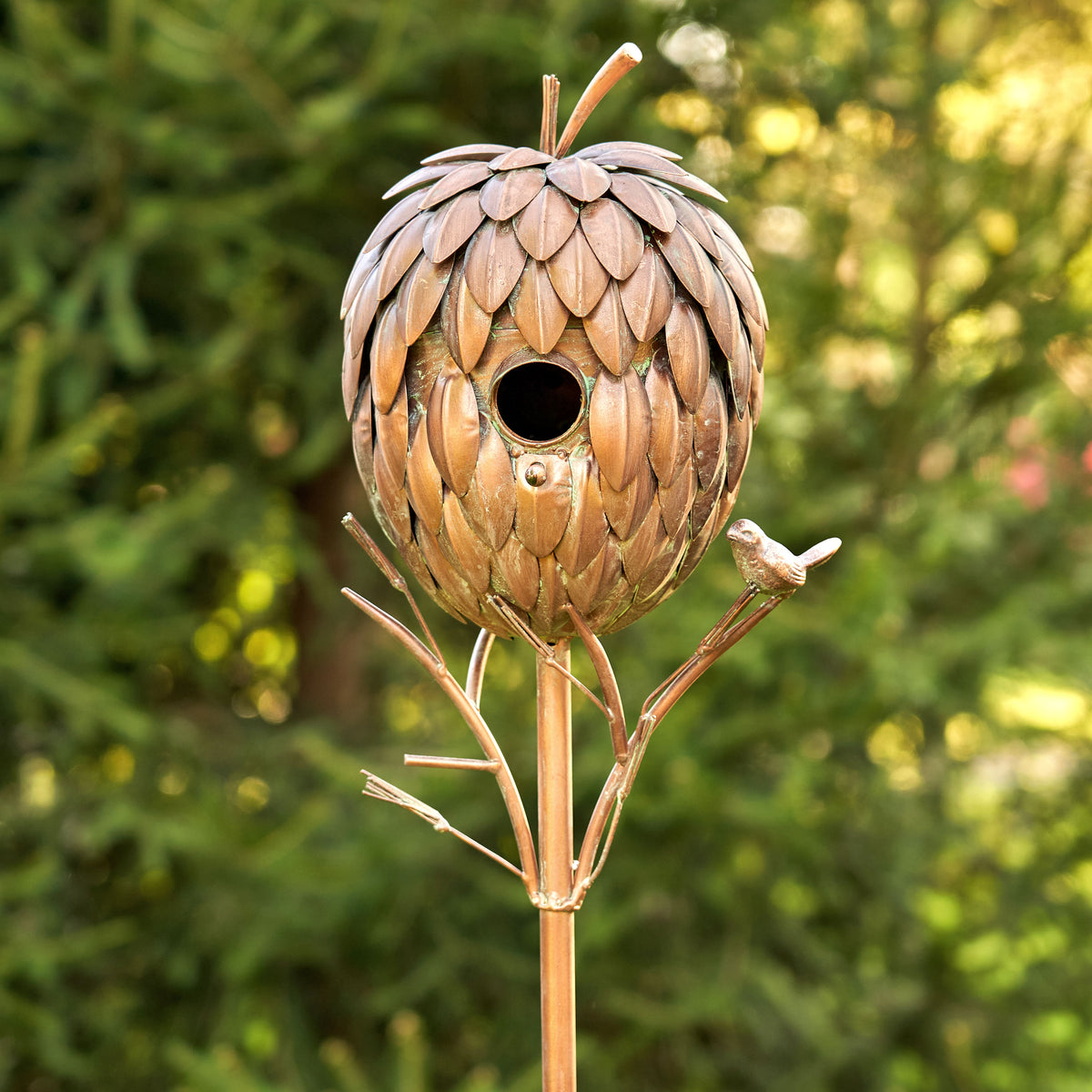 Decorative birdhouse shaped like a pine cone on a stand with a blurred green background