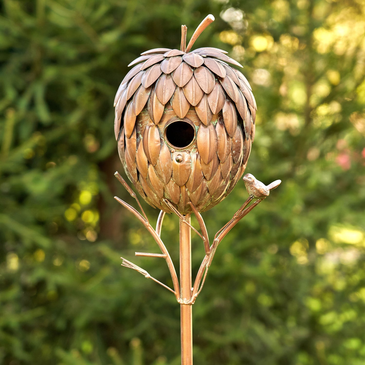 Decorative birdhouse shaped like a pine cone on a stand with a blurred green background