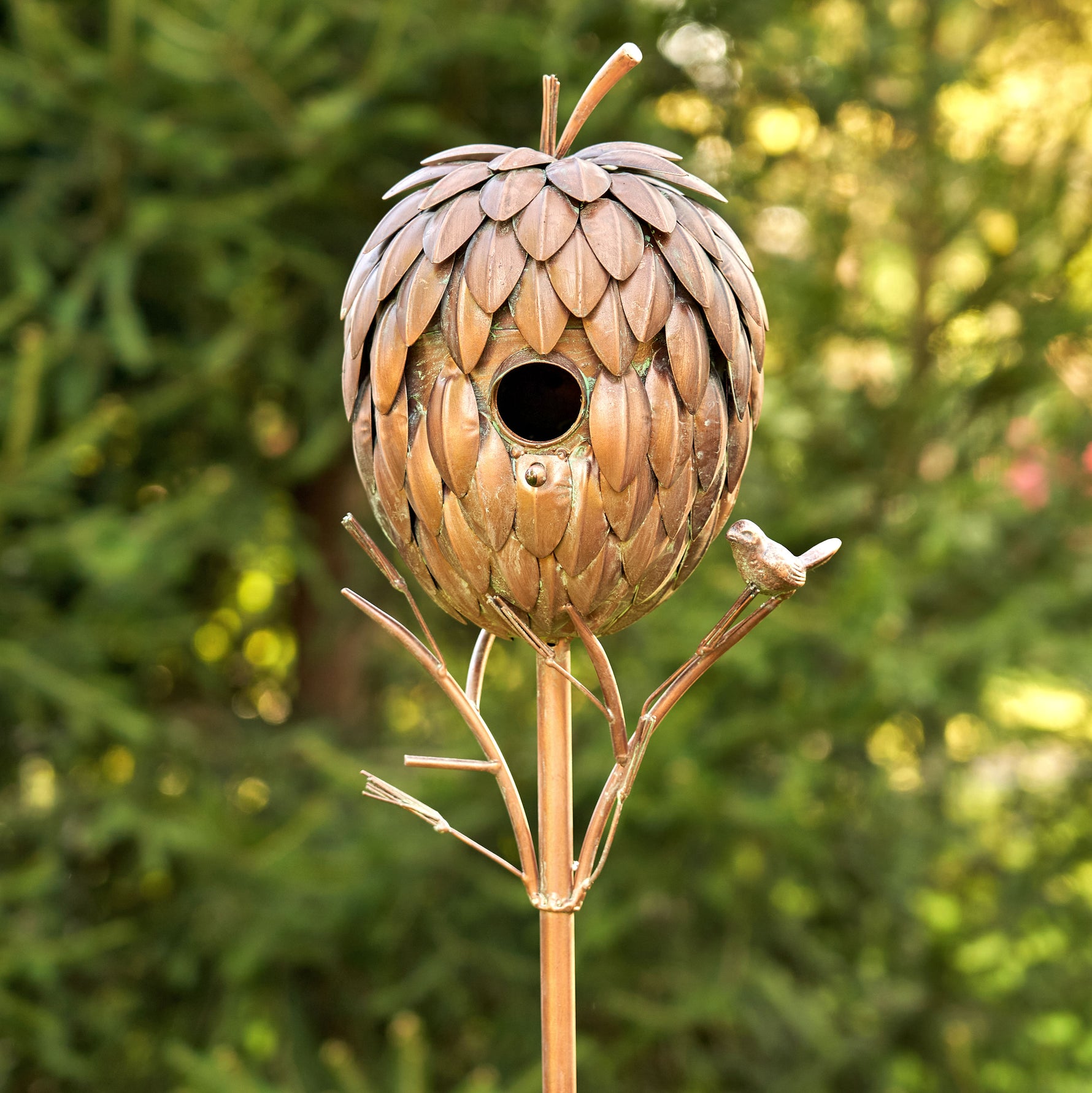 Decorative birdhouse shaped like a pine cone on a stand with a blurred green background
