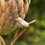 Bronze sculpture of a bird perched on a branch with a blurred green background