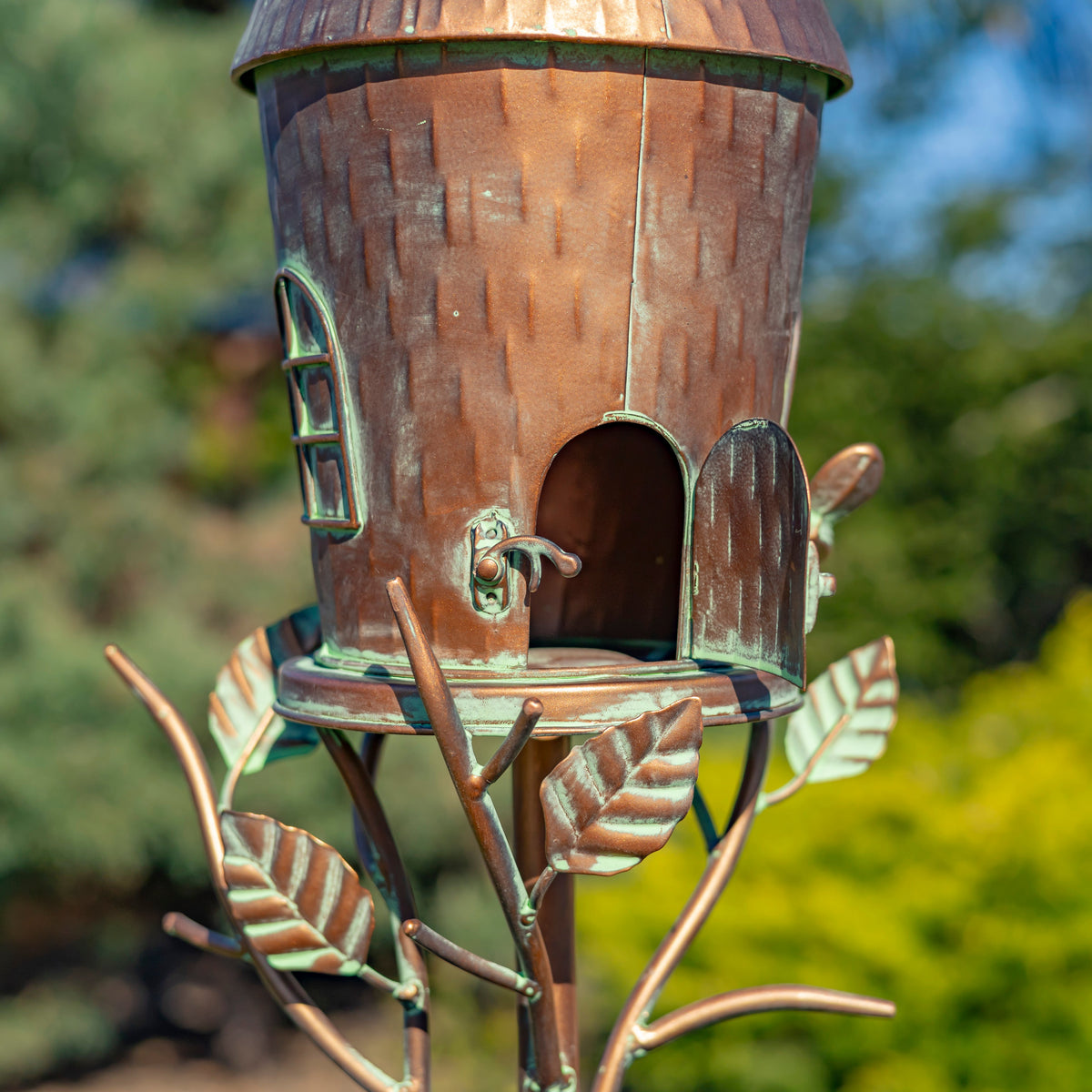 Decorative copper birdhouse with leaf designs on a blurred green background
