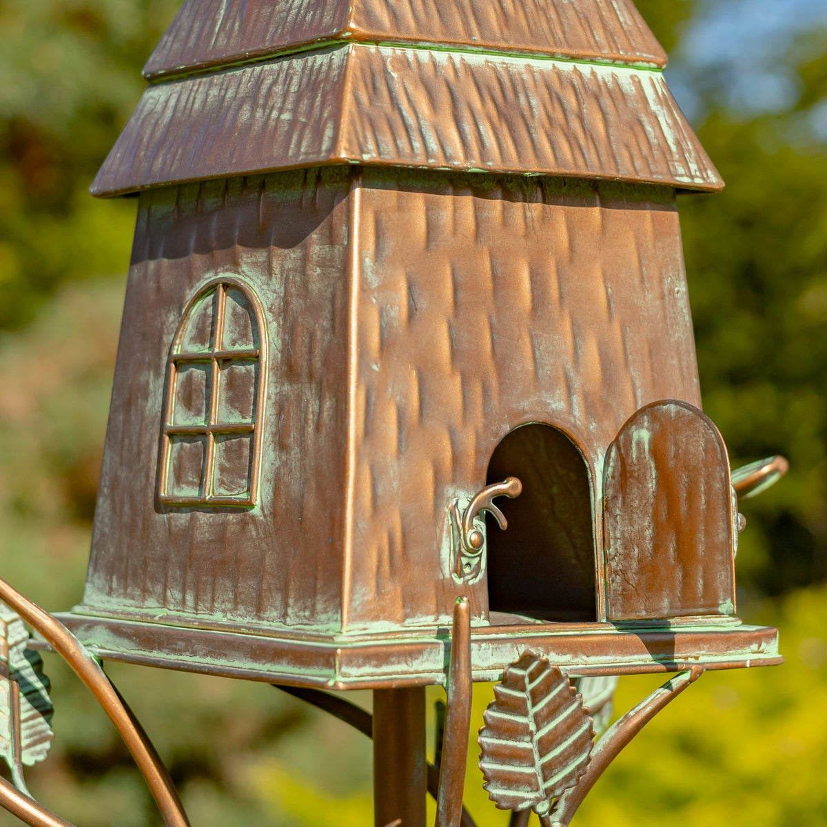 Bronze birdhouse with a textured finish against a blurred natural background