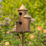 Rust-colored birdhouse with multiple holes on a stand against a blurred garden background