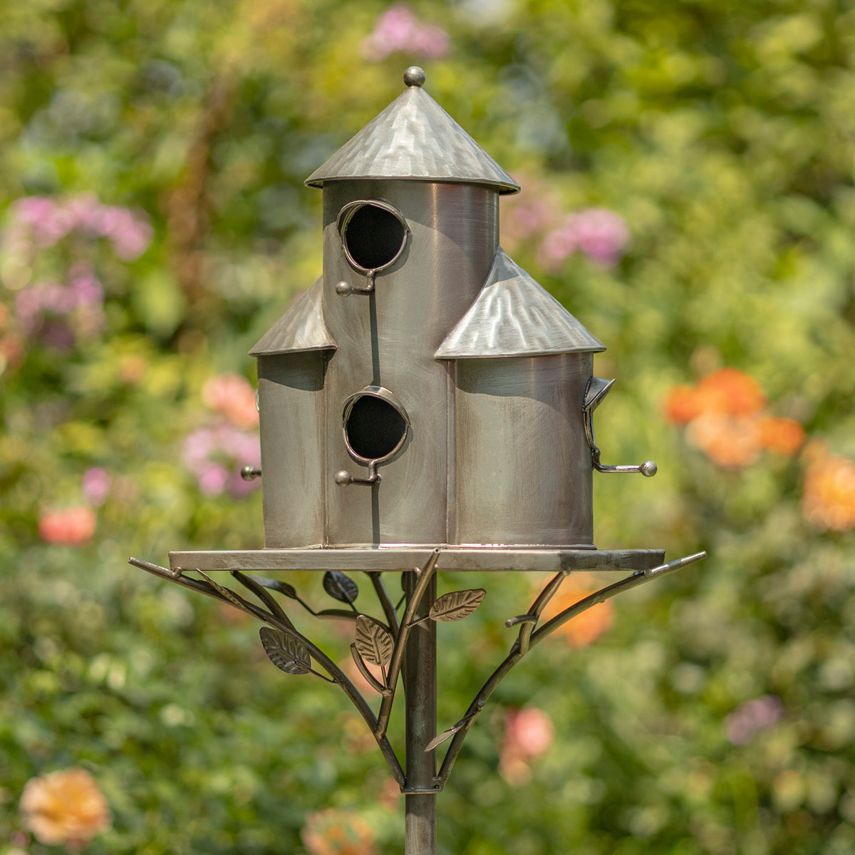 Metal birdhouse with a decorative stand against a blurred garden background