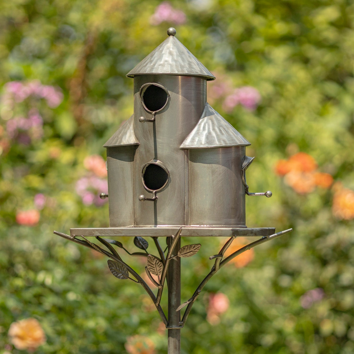 Metal birdhouse with a decorative stand against a blurred garden background