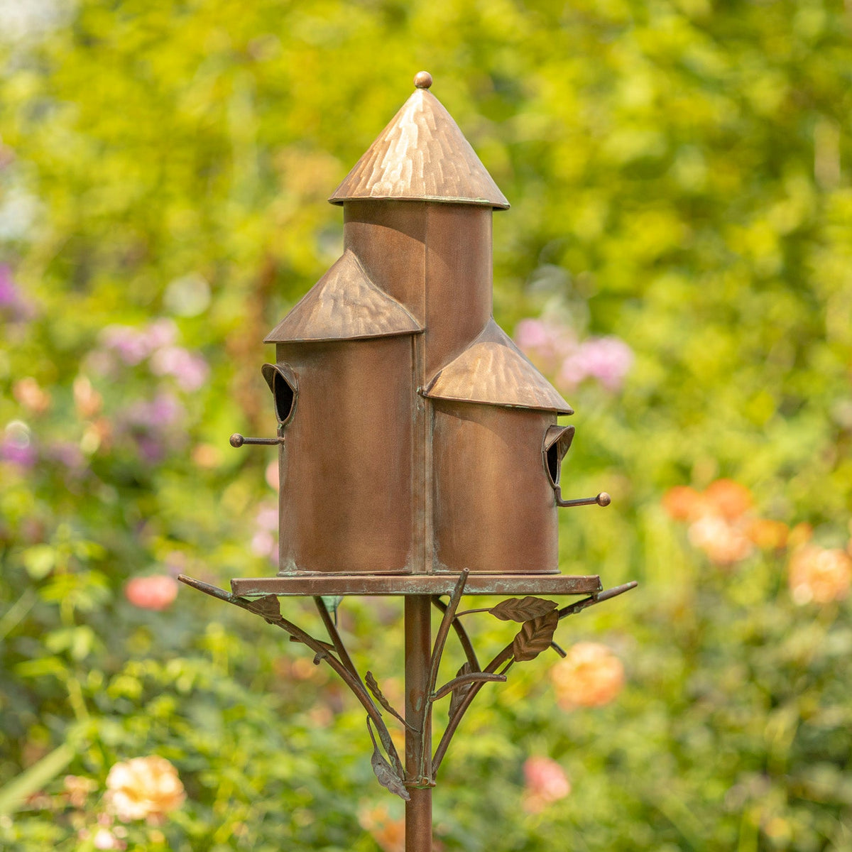 Decorative copper birdhouse on a stand with a blurred garden background