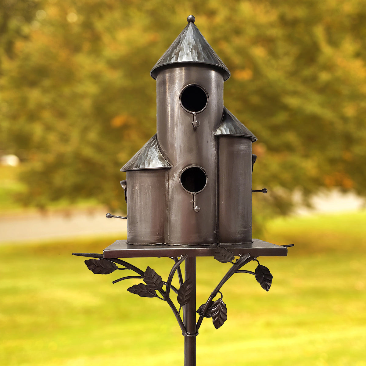 Decorative metal birdhouse on a stand with a blurred green background