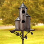 Decorative metal birdhouse on a stand with a blurred green background
