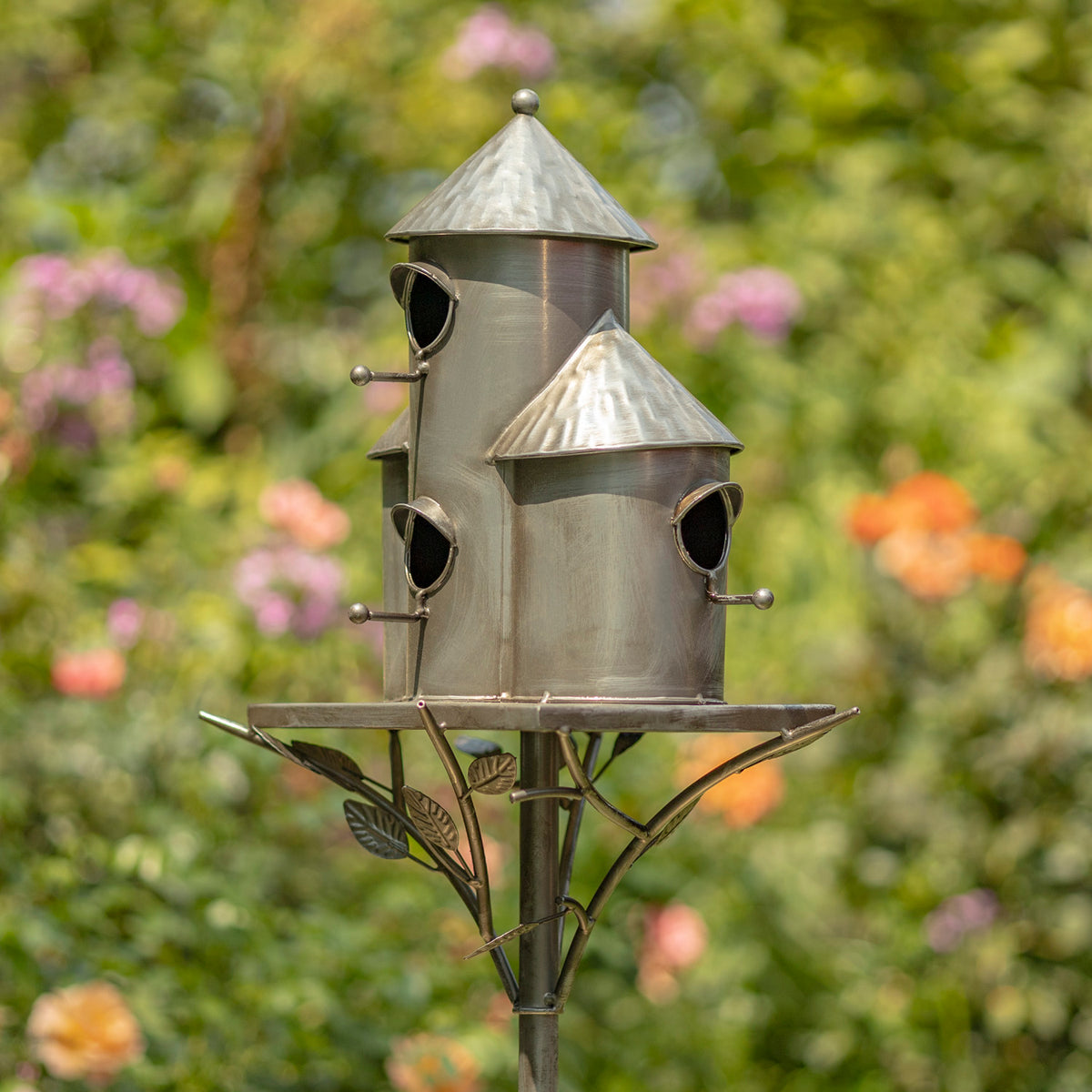 Metal birdhouse with multiple compartments on a stand against a blurred garden background