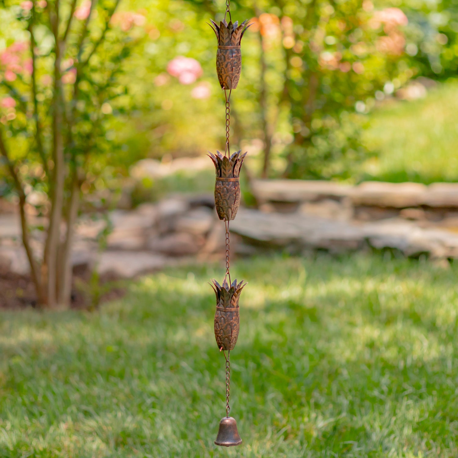 Decorative wind chime hanging in a garden with greenery and a wooden bench in the background.