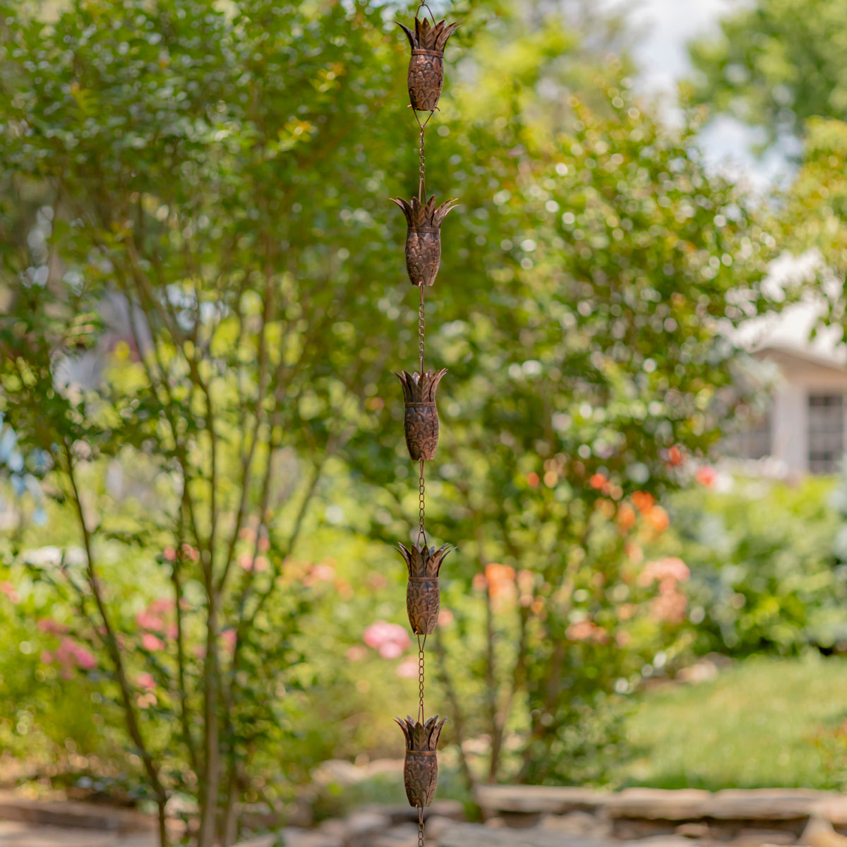 Decorative wind chime hanging in a garden with trees and flowers in the background