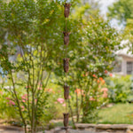 Decorative wind chime hanging in a garden with trees and flowers in the background