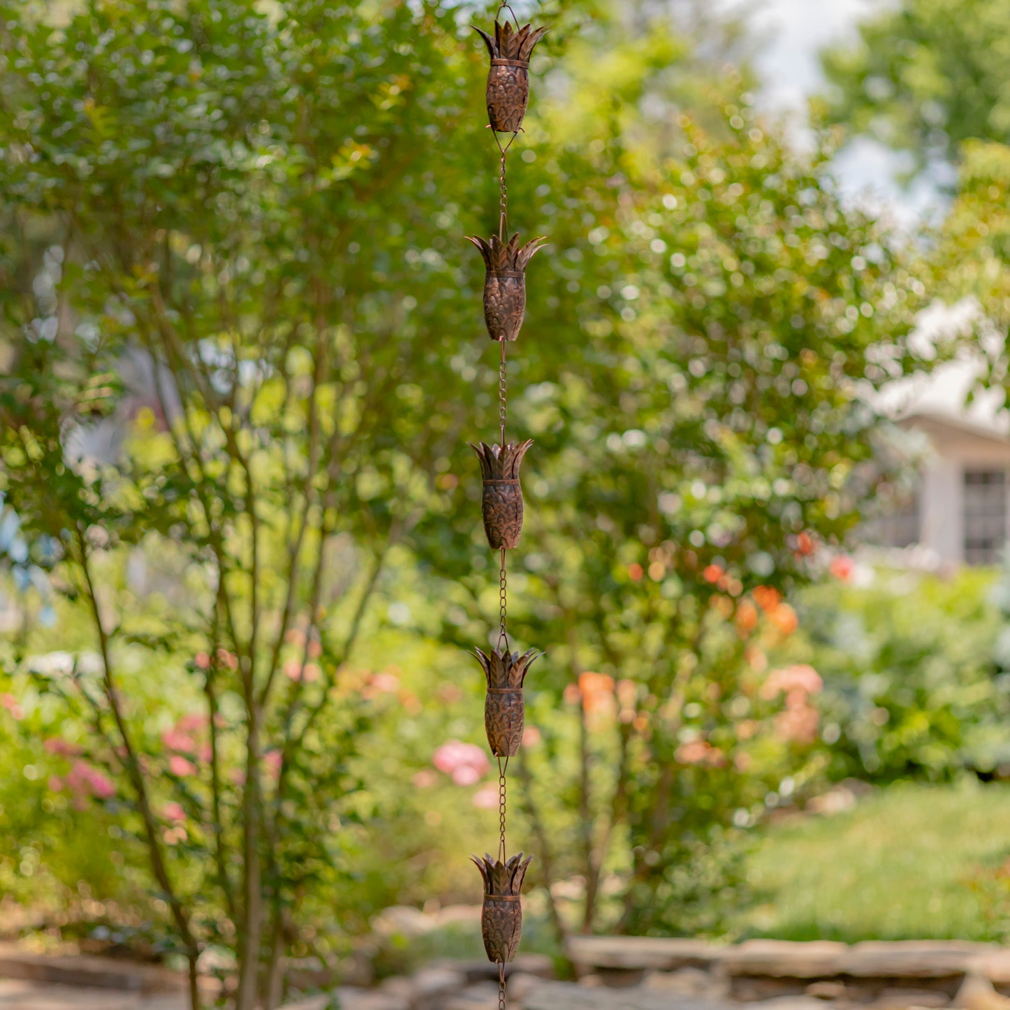 Decorative wind chime hanging in a garden with trees and flowers in the background