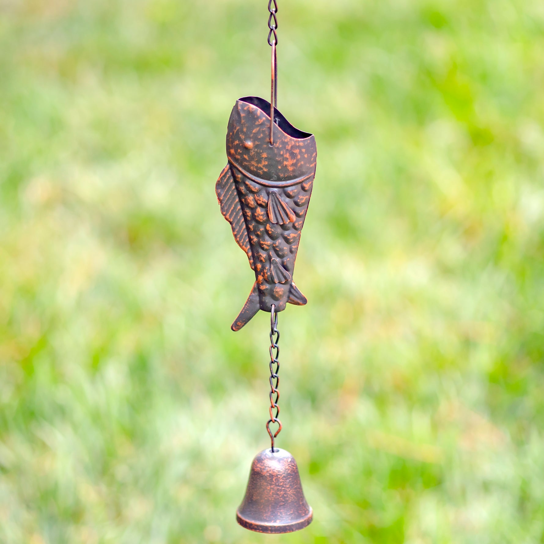 Bronze fish-shaped wind chime with a bell against a blurred green background