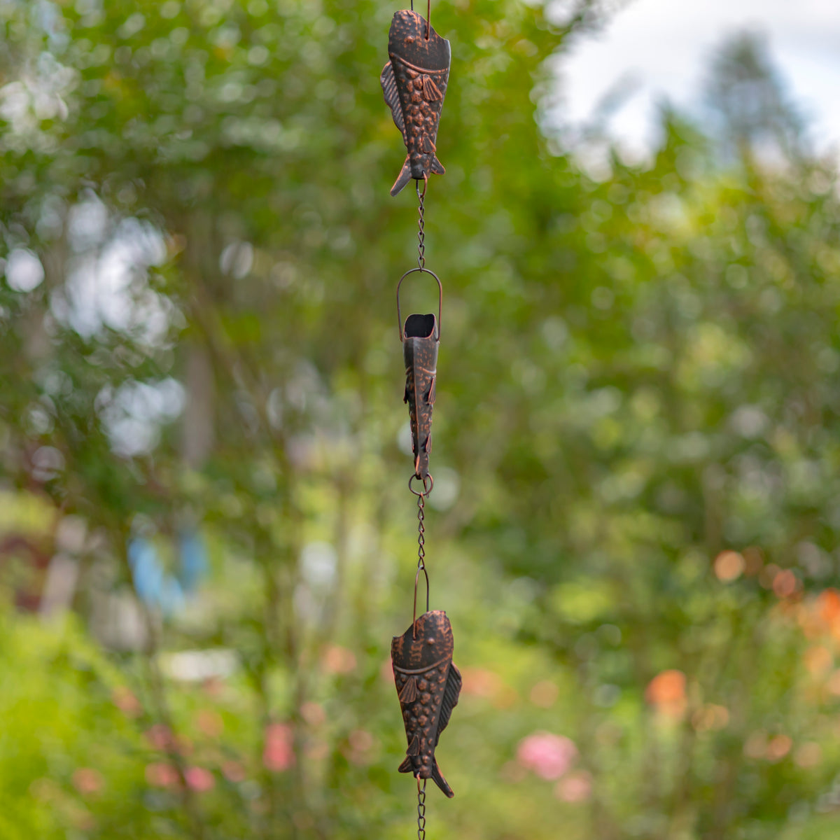 Decorative fish-shaped wind chime against a blurred green garden background