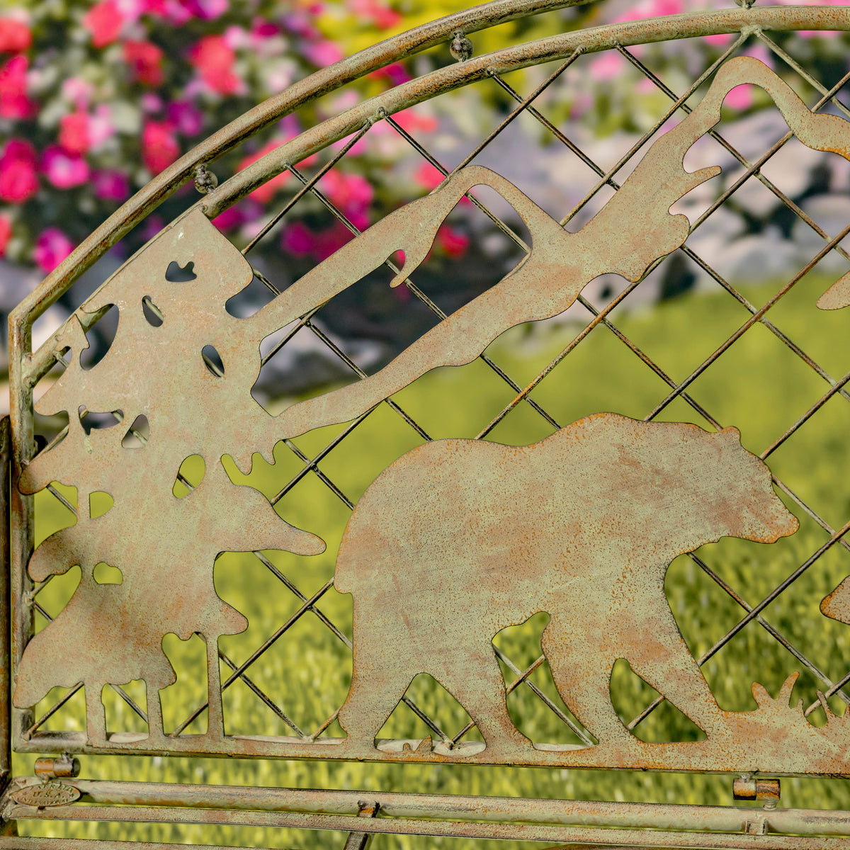 Decorative metal gate with bear and tree cutouts in a garden setting
