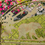 Decorative metal gate with bear and tree cutouts in a garden setting