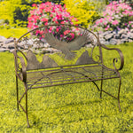 Decorative metal bench with eagle design on a grassy area with flowers in the background