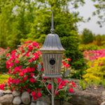 Decorative birdhouse on a stand with flowers and trees in the background