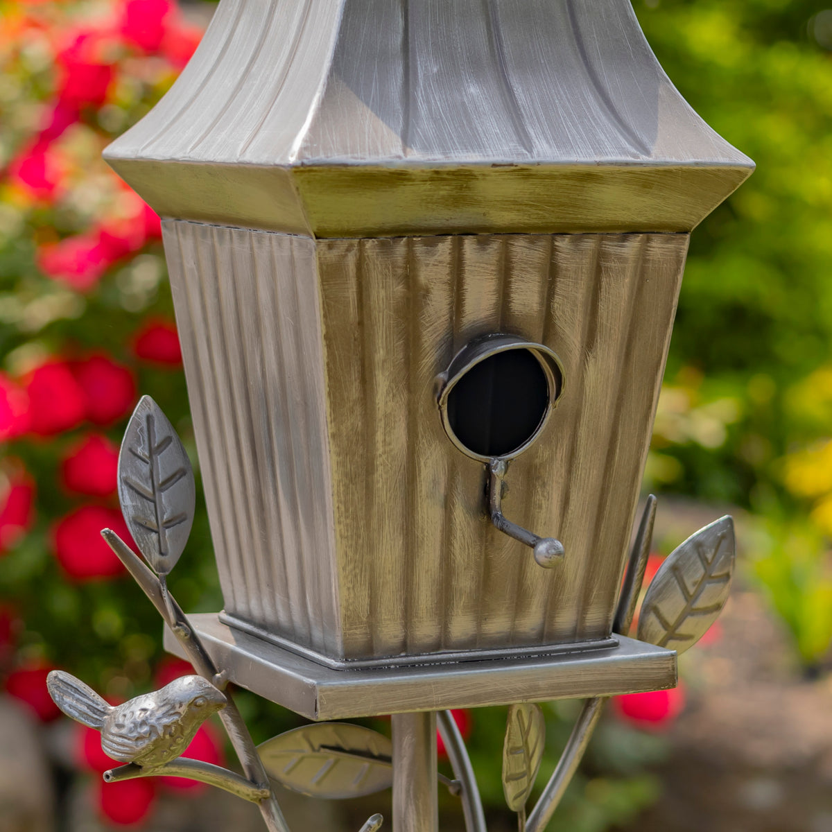 Decorative metal birdhouse with leaf designs on a blurred garden background